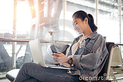 Young Asian female tourist look at smart phone with her laptop at airport Stock Photo