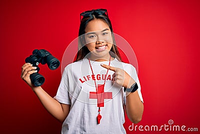 Young asian lifeguard girl wearing t-shirt with red cross using whistle and binoculars very happy pointing with hand and finger Editorial Stock Photo