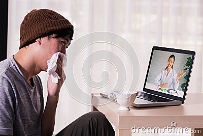 Young Asian male patient with sickness using laptop to video call conferencing with doctor at home. Medical Stock Photo