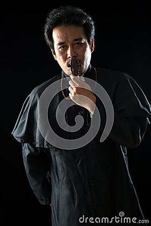 Young Asian male Priest with black uniform holding crucifix rosary Stock Photo