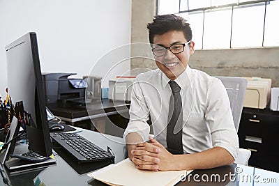 Young Asian male professional at desk smiling to camera Stock Photo