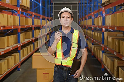 Young asian male worker wearing helmet using talki walki in modern warehouse Stock Photo