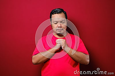 Young Asian man close his eyes face down and grasping his hands, wishful expression Stock Photo