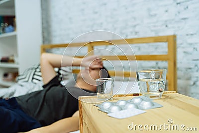 Young Asian man feeling sick and ill lying on bed with medicines tablets and pills on table Stock Photo