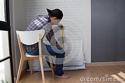 Young Asian man glueing wallpapers on the wall at home. Stock Photo