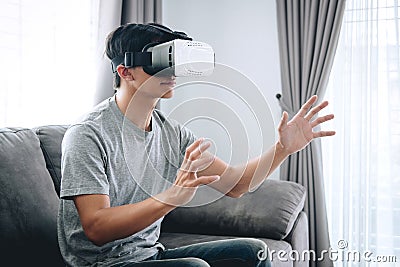 Young asian man having fun wearing playing virtual reality headset glasses to enjoying in holiday at home, 3D gadget technology, Stock Photo