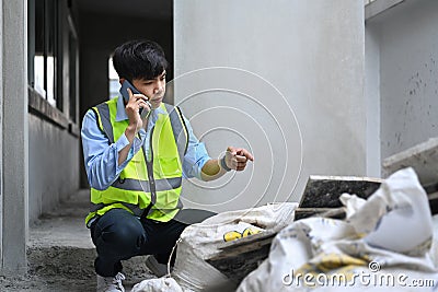 Young asian man inspectors talking on mobile phone and checking building material at construction site Stock Photo