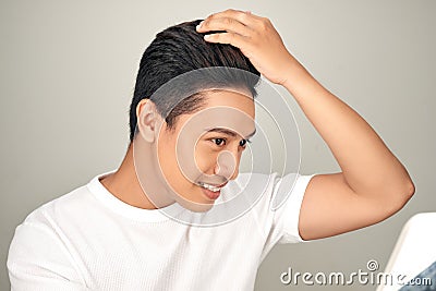 Young Asian man is lokking in mirror and touching his hair on white background Stock Photo