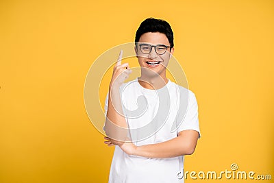 Young Asian man wearing a white T-shirt and glasses. He pointed a finger with a happy face. Isolated background Stock Photo