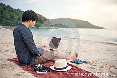 Young Asian man working with laptop on the beach Stock Photo