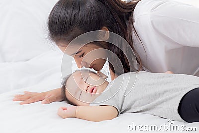 Young asian mother kiss cheek of little baby girl with tender on bed in the bedroom, mom love newborn and care. Stock Photo
