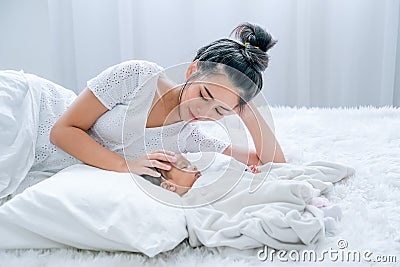 Young Asian mother lie on white bed and take care her newborn baby Stock Photo
