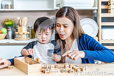 Young asian mother and little son enjoy to play wooden jigsaw puzzle together in area of kitchen of their house and they look Stock Photo