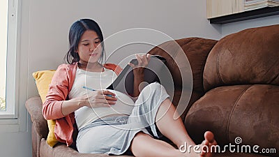 Young Asian Pregnant woman drawing baby in belly in notebook. Mom feeling happy smiling positive and peaceful while take care Stock Photo