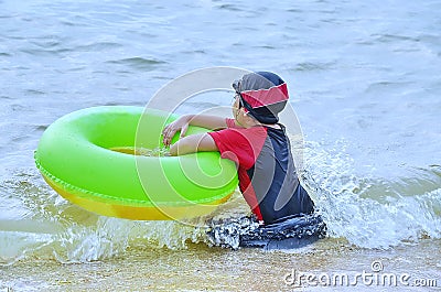 Young Asian sits in the surf on an ocean beach with her donut. Stock Photo