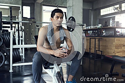 Young asian sporty man tired sitting with towel after gym workout in fitness Stock Photo