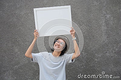 Young asian student with glasses and fedora hat standing holding white board and smiling, blank board concept Stock Photo