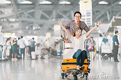 Asian tourist couple happy and excited together for the trip, girlfriend sitting and cheering on baggage trolley or luggage cart Stock Photo