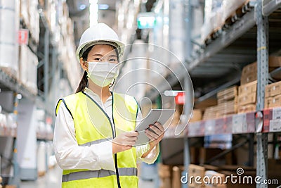Young asian woman auditor or trainee staff wears mask working during the COVID pandemic in store warehouse shipping industrial. Stock Photo