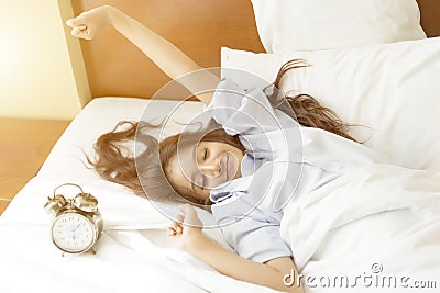 Young Asian woman in bed trying to wake up with alarm clock Stock Photo