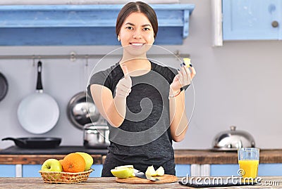 A young asian woman in a black t-shirt makes a fit breakfast and tries to taste a piece of apple Stock Photo