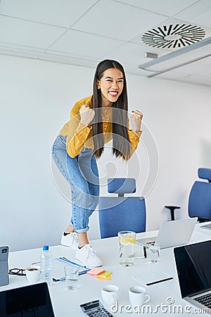 Young Asian woman clenching her fists in joy at office Stock Photo