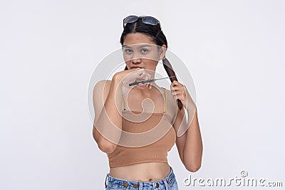 A young asian woman considers cutting her long locks of hair with a pair of scissors. Isolated on a white background Stock Photo