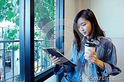 Young asian woman holding a coffee cup and digital tablet sitting in room, lifestyle, working from home, adult online education Stock Photo