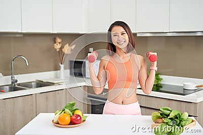 Young Asian woman holding dumbell and wearing sportive clother in kitchen Stock Photo