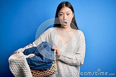 Young asian woman holding wicker laundry basket doing domestic chores scared in shock with a surprise face, afraid and excited Editorial Stock Photo