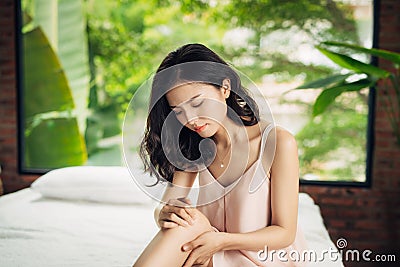 Young asian woman with leg pain sitting on bed Stock Photo