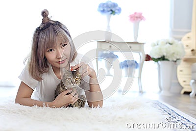 A young Asian woman lounging with a cat in a living room with a white fur rug. Woman and cat looking forword Stock Photo