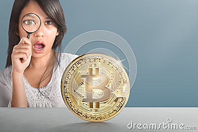 Young asian woman with magnifier looking at golden bitcoin Stock Photo