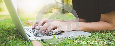Young asian woman`s legs on the green grass with open laptop. Girl`s hands on keyboard. Distance learning concept. Stock Photo
