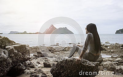 Young asian woman sitting on a rock near the sea,looked to the sea,chill out of summer,rest time,light and flare effect added Stock Photo