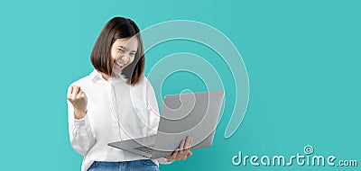 Young Asian woman smiling holding laptop computer with fist hand and excited for success on light blue background Stock Photo