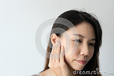 Young Asian woman with sore ear suffering from otitis over white background. Girl touch her ear with pain. Ear problem Stock Photo
