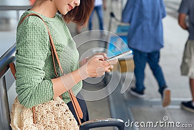 Young asian woman standing with suitcase and looking at mobile phone while waiting at the airport Stock Photo