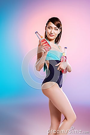 Young asian woman in swimsuit holding bottles with refreshing summer drinks and looking away Stock Photo