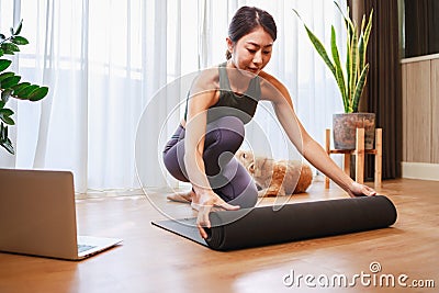 Young Asian woman unrolling roll black yoga mat for online training yoga with her dog at home Stock Photo