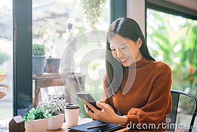 Young Asian woman using phone at a coffee shop happy and smile. Stock Photo