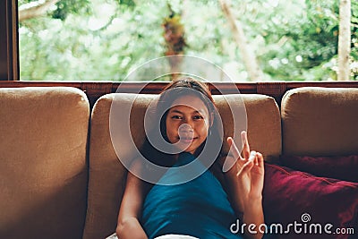 Young Asian woman during vacation relaxing on the sofa with big window behind her. woman on summer vacation in Bali Stock Photo