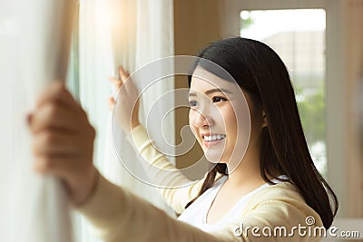 Young asian woman wake up in early morning and open curtain looking at nice view feeling freshness with smile face and happiness Stock Photo