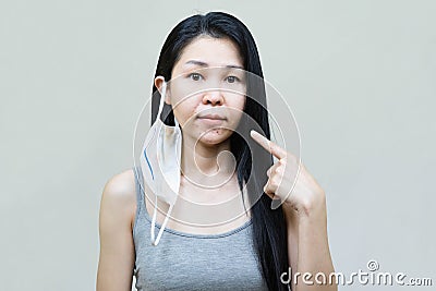 Young asian woman wearing medical face mask her hand point at pimple on chin,Skin allergy,acne from wearing a mask Stock Photo