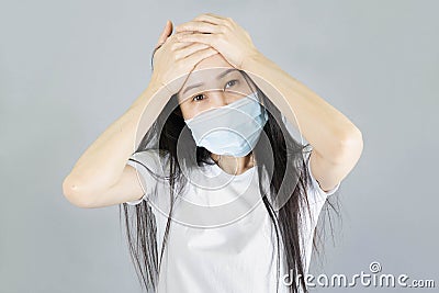 Young Asian woman wearing medical face mask and white t shirt her hand on the head. isolated on gray background,health care Stock Photo