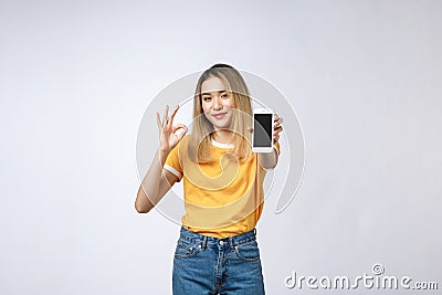 Young Asian woman wearing in yellow shirt is showing ok sign on white background, holding mobile phone, smiling, Stock Photo