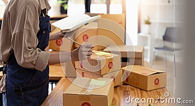 Young asian woman writing address on parcel box at home for delivery order to customer, shipping and logistic, merchant Stock Photo