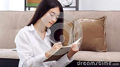 Young asian woman writing on notebook paper at home office Stock Photo