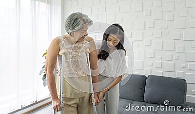 Young asian woman help her grandma walk by using axilla crutches. Senior gray hair woman exercise and practice walking at home Stock Photo