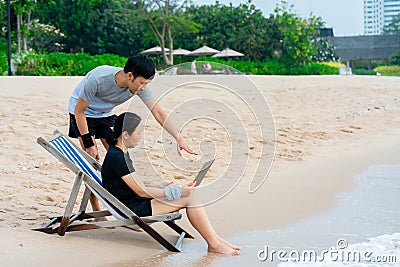 Young Asians sit on a laptop video chatting on a laptop, in a chair by the sea, comfortably, Stock Photo